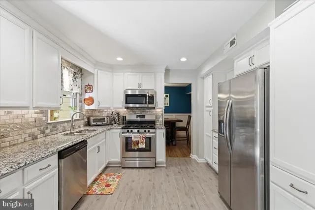 a kitchen with stainless steel appliances granite countertop a refrigerator a sink dishwasher a stove with wooden cabinets and floor