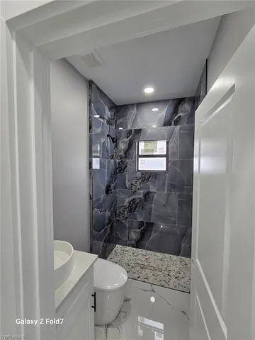 a bathroom with a granite countertop sink a toilet a mirror and shower