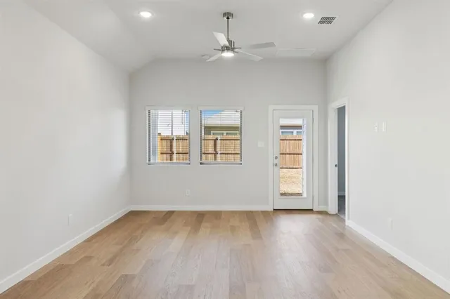 an empty room with wooden floor ceiling fan and windows