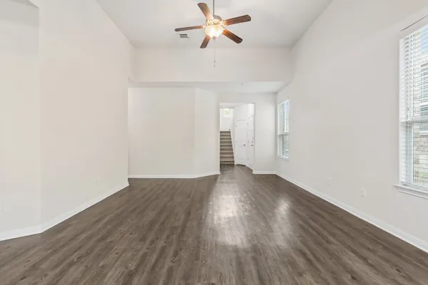 an empty room with wooden floor chandelier fan and windows