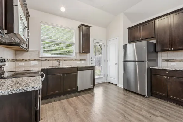 a kitchen with granite countertop stainless steel appliances a refrigerator cabinets and wooden floor
