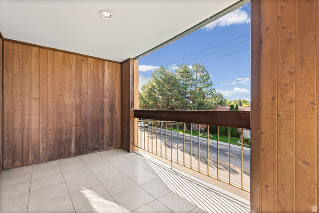 2244 North Canyon Road, Unit 212 Provo, UT 84604 - Photo 8 of 31 Spacious covered balcony with tile flooring, wood-finish paneled walls, and metal railing overlooking landscaped grounds and mature trees