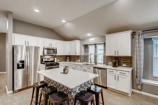 a kitchen with stainless steel appliances a stove a sink a refrigerator and white cabinets with wooden floor