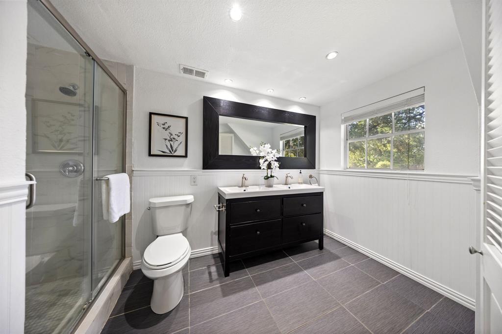 3060 Timberview Road Dallas, TX 75229 - Photo 21 of 39 Contemporary bathroom featuring a dark wood-finish dual vanity with a light-colored countertop, a glass-enclosed shower, a large framed mirror, and a window providing natural light