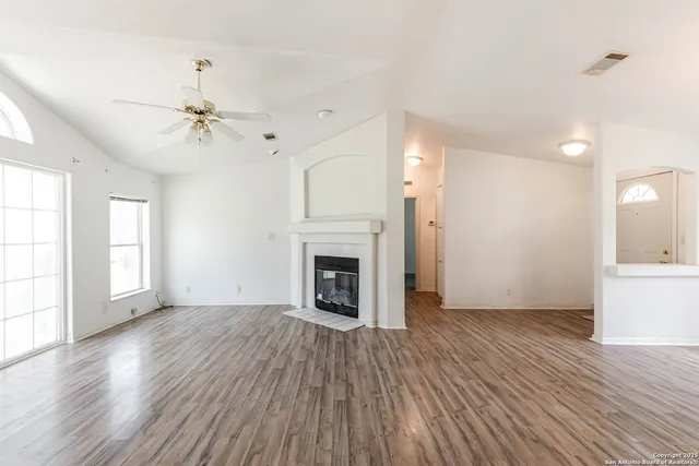 an empty room with large windows a fireplace a ceiling fan and wooden floor