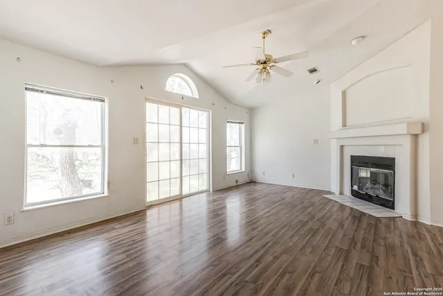 an empty room with windows fireplace and wooden floor