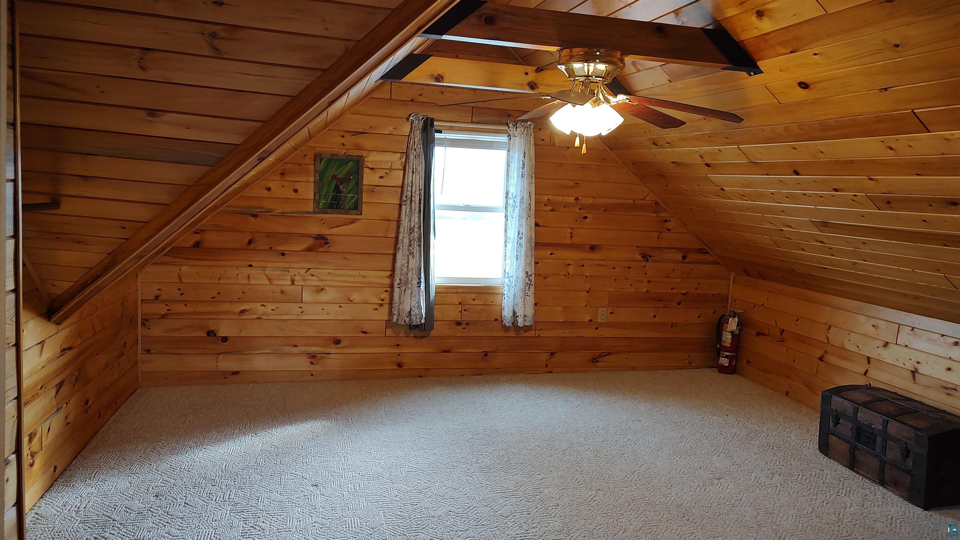 2585 Hautala Road Iron River, WI 54847 - Photo 14 of 28 Carpeted room featuring natural wood paneling on walls and ceiling, a ceiling fan with integrated lighting, and a window with sheer curtains