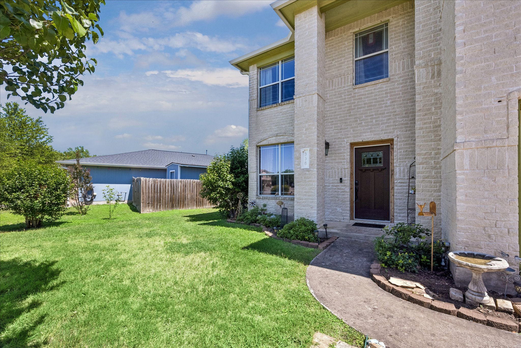 338 Spring Branch Loop Kyle, TX 78640 - Photo 2 of 36 A cream brick facade offers a welcoming entry framed by verdant shrubs and a well-tended lawn.