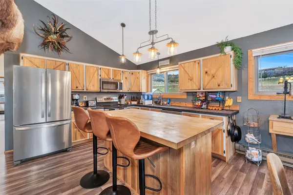 a kitchen with stainless steel appliances granite countertop a refrigerator a sink dishwasher a stove and a dining table with wooden floor