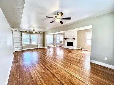 an empty room with wooden floor ceiling fan and windows