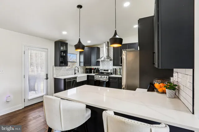 a kitchen with stainless steel appliances kitchen island granite countertop a refrigerator a oven a sink a dining table and chairs with wooden floor