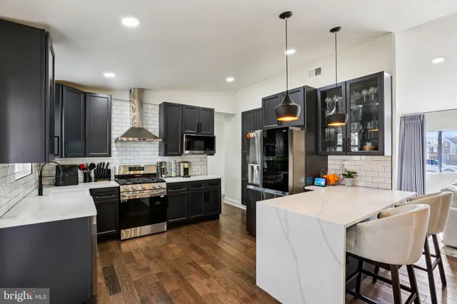 a kitchen with stainless steel appliances kitchen island granite countertop a refrigerator a stove top oven and a center island with wooden floor