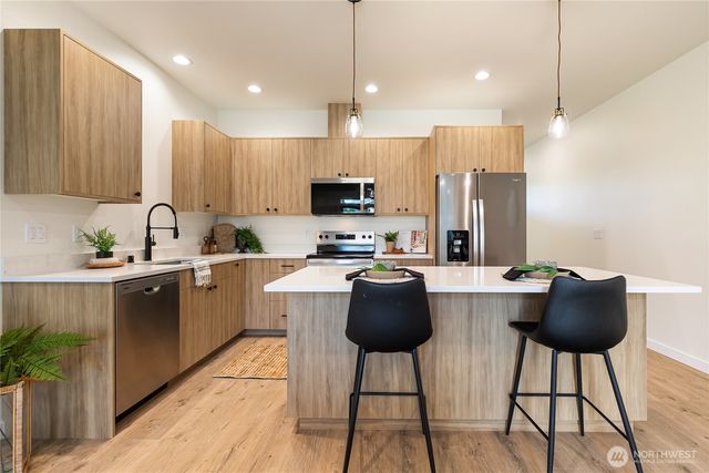 a kitchen with stainless steel appliances kitchen island granite countertop a refrigerator a stove a sink a microwave a dining table and chairs with wooden floor
