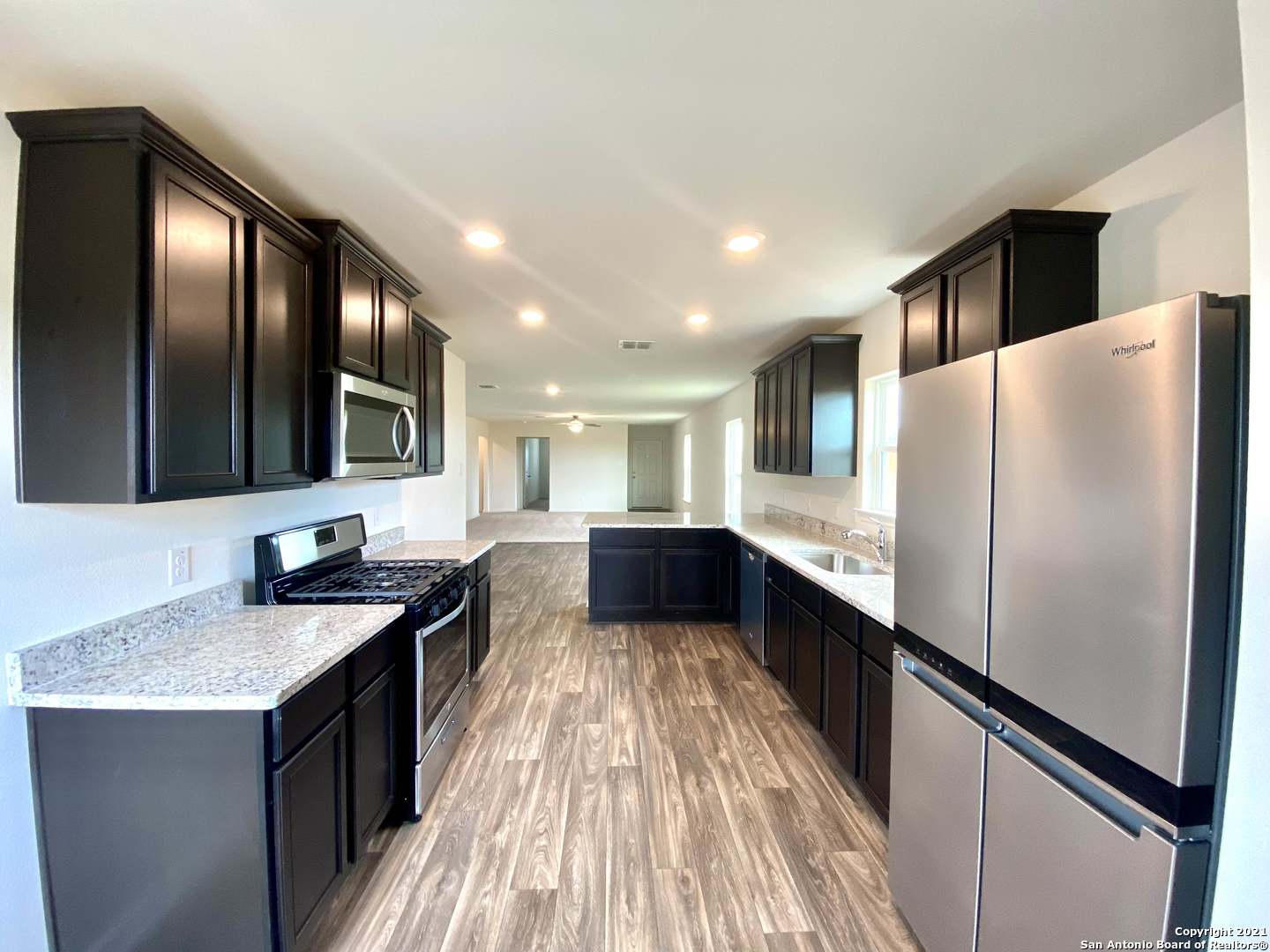 a kitchen with granite countertop a refrigerator a sink a stove and wooden cabinets