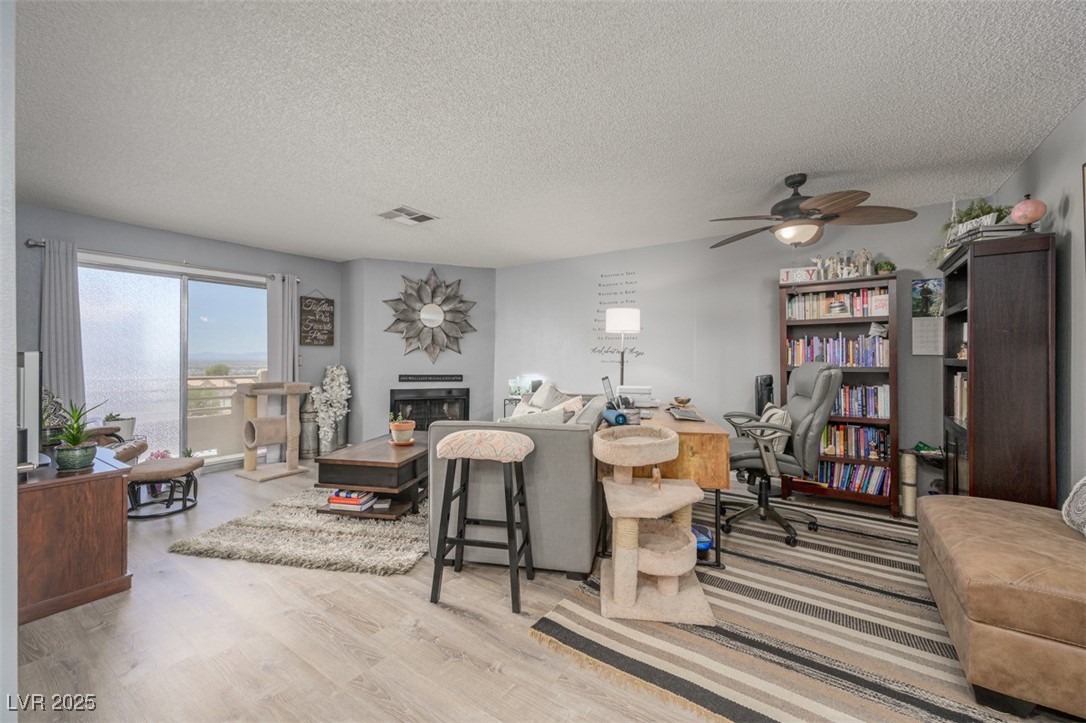 2240 Highpointe Drive, Unit 203 Laughlin, NV 89029 - Photo 17 of 38 Living area with ceiling fan, a textured ceiling, a glass covered fireplace, wood finished floors, and visible vents