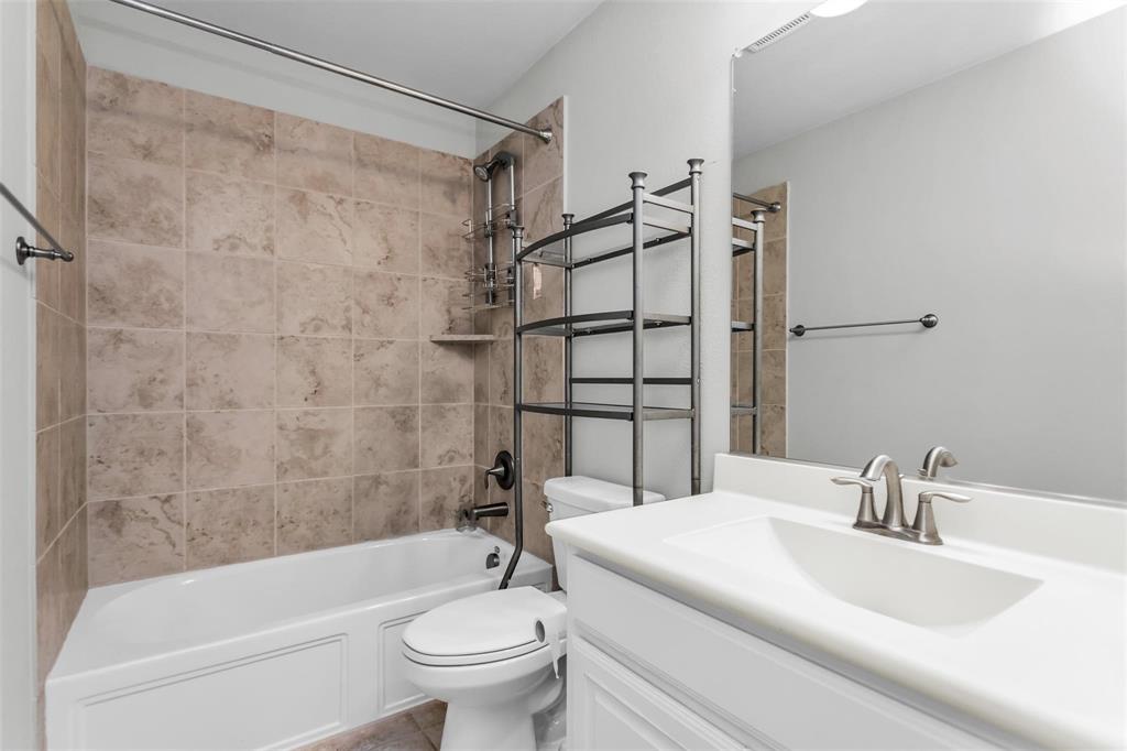 6333 Hall Road Frisco, TX 75034 - Photo 31 of 38 Bathroom featuring a white vanity with an integrated sink, brushed nickel faucet, large wall mirror, and a shower-tub combination with natural stone tile surround