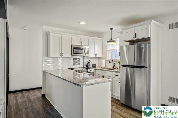 a kitchen with stainless steel appliances granite countertop a refrigerator a stove a sink and white cabinets with wooden floor