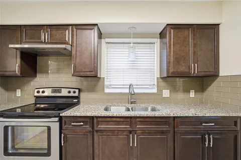 a kitchen with granite countertop a sink a stove and cabinets