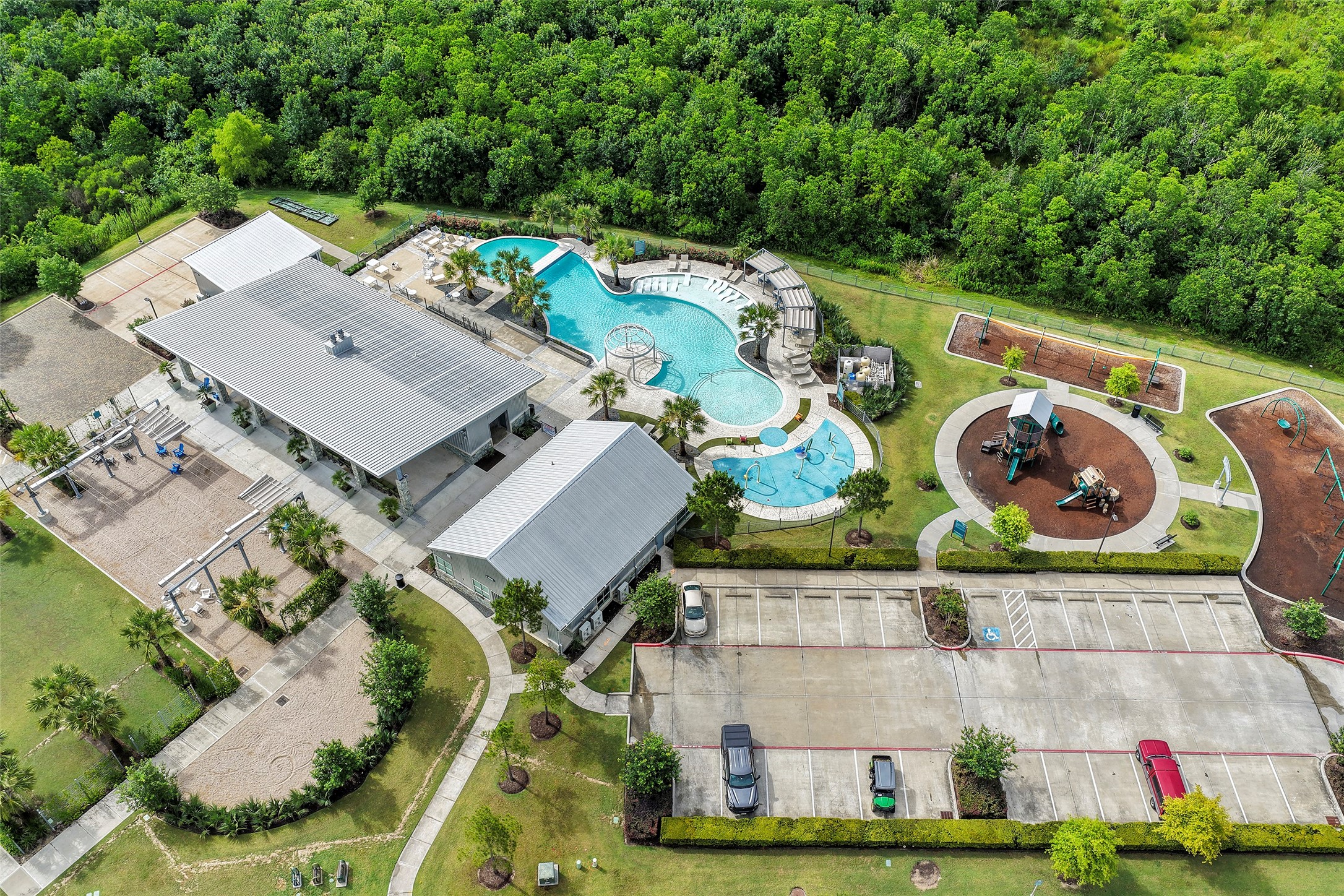 10603 Whitejacket Conroe, TX 77385 - Photo 34 of 42 This aerial photo of the community amenities, showcases a vibrant community recreation area with a large, inviting pool, adjacent playground, and spacious parking lot. Surrounded by lush greenery, the facility includes covered structures for gatherings and ample space for outdoor activities, providing an ideal setting for family fun and relaxation.