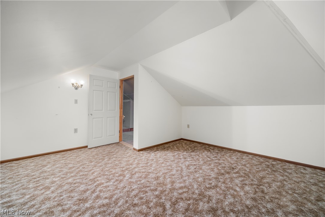 51488 Peck Wadsworth Road Wellington, OH 44090 - Photo 45 of 50 Spacious room featuring sloped ceilings, light-toned patterned carpeting, a white paneled door, and a wall-mounted light fixture