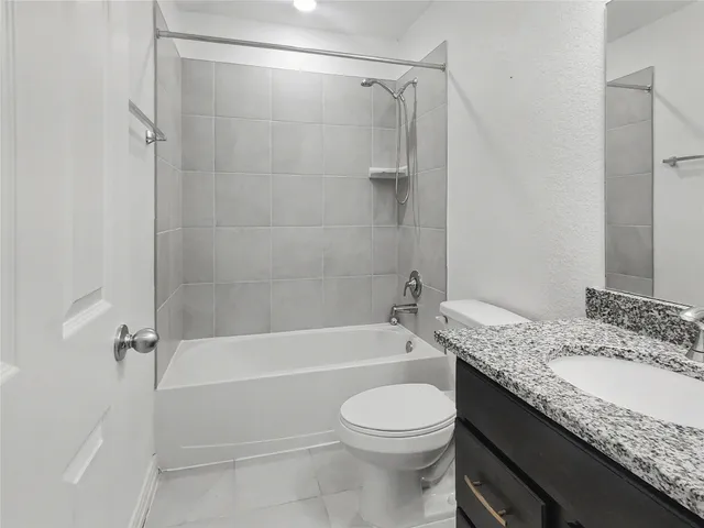 a bathroom with a granite countertop bathtub shower sink vanity and toilet