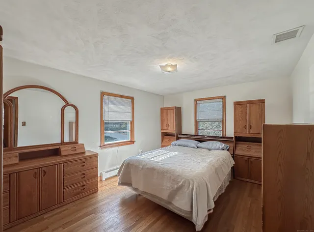 a bedroom with a bed and a dresser with wooden floor
