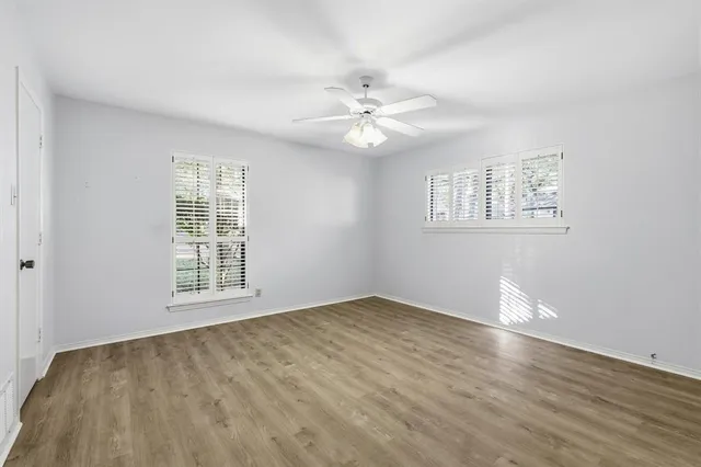 an empty room with wooden floor chandelier fan and windows