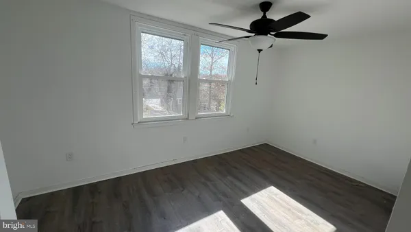 an empty room with wooden floor ceiling fan and windows
