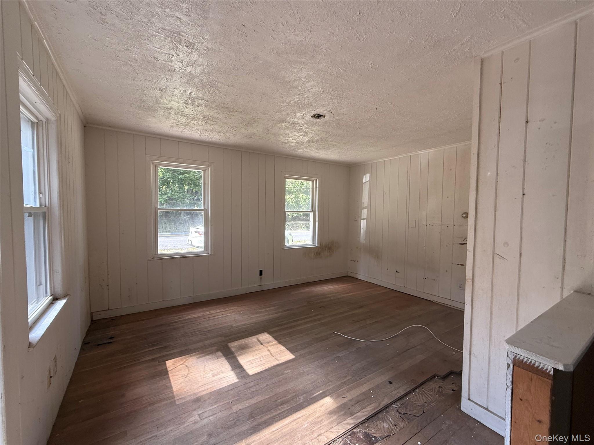 3968 Old Crompond Road Cortlandt Manor, NY 10567 - Photo 5 of 17 Unfurnished dining area featuring wood-type flooring, wood walls, and a textured ceiling