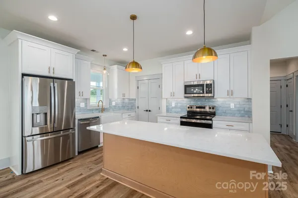 a kitchen with stainless steel appliances a stove a refrigerator a sink and a wooden floor