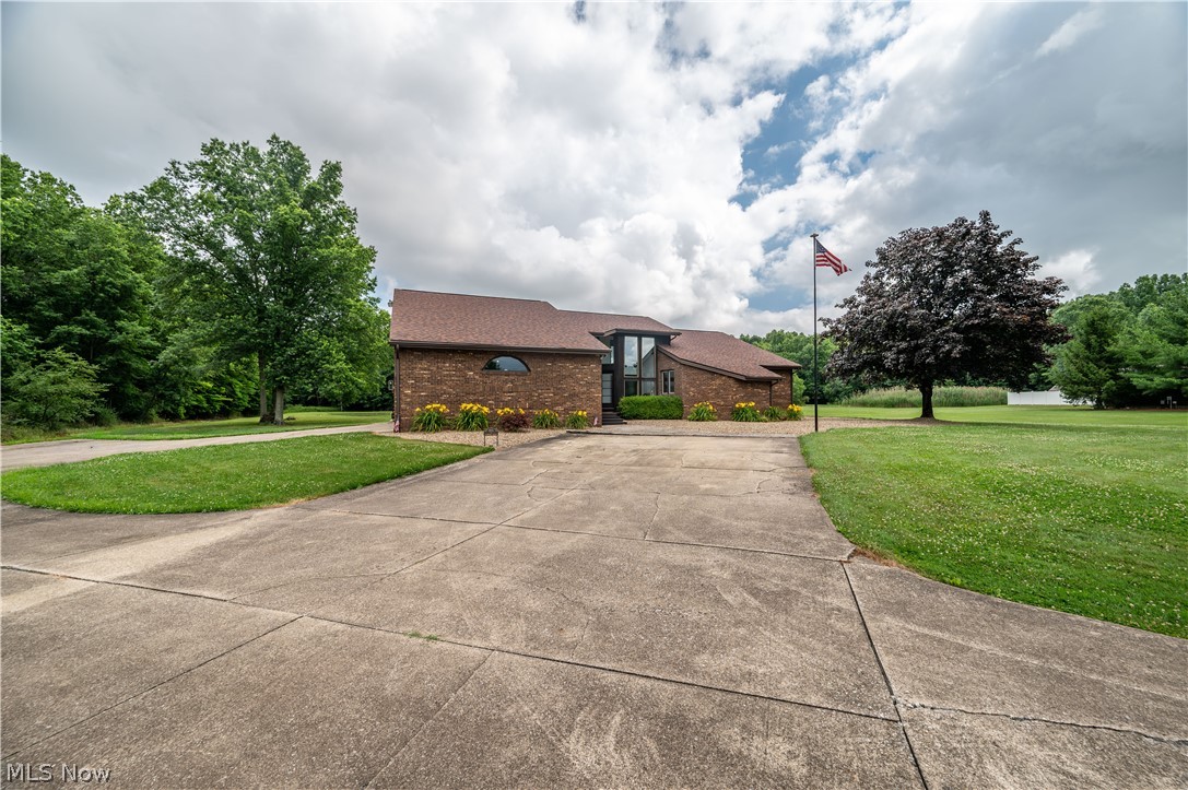 405 Airport Road Northwest Warren, OH 44481 - Photo 2 of 50 Brick exterior property featuring a substantial concrete driveway, mature trees, and a flagpole