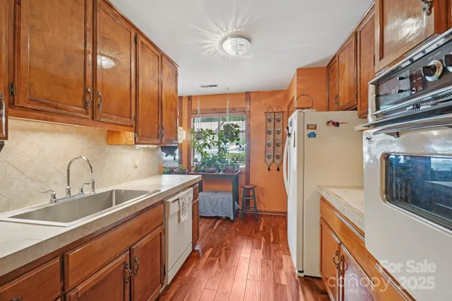 a kitchen with stainless steel appliances granite countertop a refrigerator a sink dishwasher a stove and white countertops with wooden floor