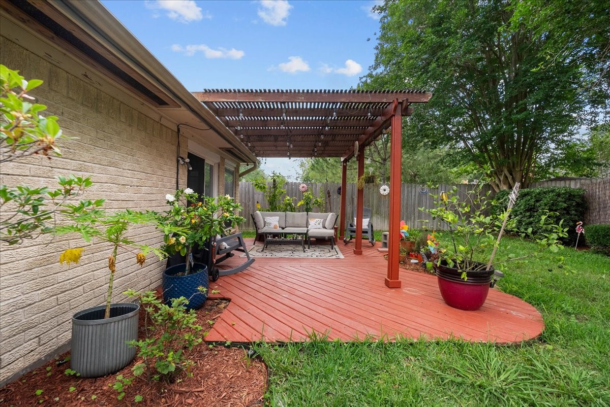 883 Silverpines Road Houston, TX 77062 - Photo 27 of 38 This backyard features a cozy wooden deck with a pergola, offering a shaded seating area. Surrounded by lush greenery and potted plants, it's an inviting space for relaxation and outdoor gatherings.