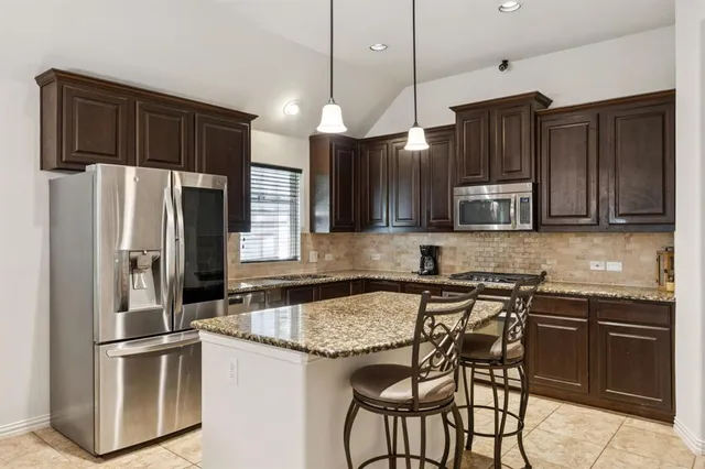 a kitchen with stainless steel appliances granite countertop a sink a stove a refrigerator and island with wooden cabinets