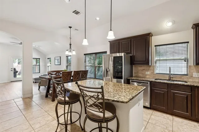 a kitchen with stainless steel appliances kitchen island granite countertop a sink a stove a refrigerator a dining table and chairs