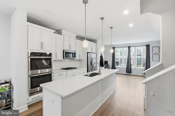 a kitchen with stainless steel appliances kitchen island granite countertop a refrigerator a stove a sink dishwasher and white cabinets with wooden floor