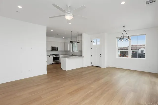 an empty room with wooden floor kitchen view and a ceiling fan