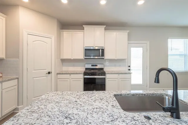 a large white kitchen with kitchen island a stove a sink a refrigerator white cabinets and wooden floor