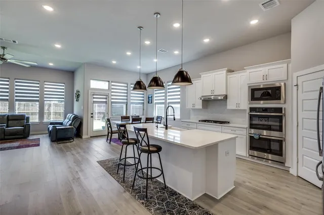 a kitchen with stainless steel appliances granite countertop a stove top oven a refrigerator a dining table and chairs with wooden floor