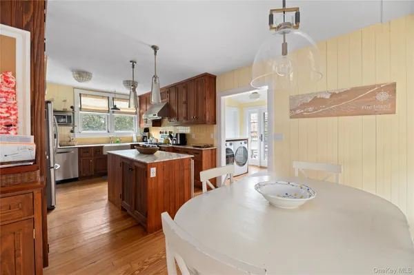 a open kitchen with stainless steel appliances granite countertop a sink a stove a refrigerator a center island a dining table and chairs with wooden floor