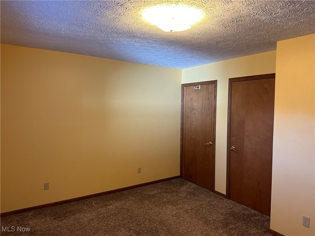 59558 Sandy Ridge Road Barnesville, OH 43713 - Photo 18 of 46 Unfurnished bedroom featuring carpet floors, multiple closets, and a textured ceiling