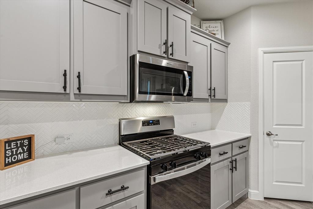 155 Texasage Street Rhome, TX 76078 - Photo 14 of 31 Kitchen featuring stainless steel appliances, gray cabinetry, tasteful backsplash, and light countertops