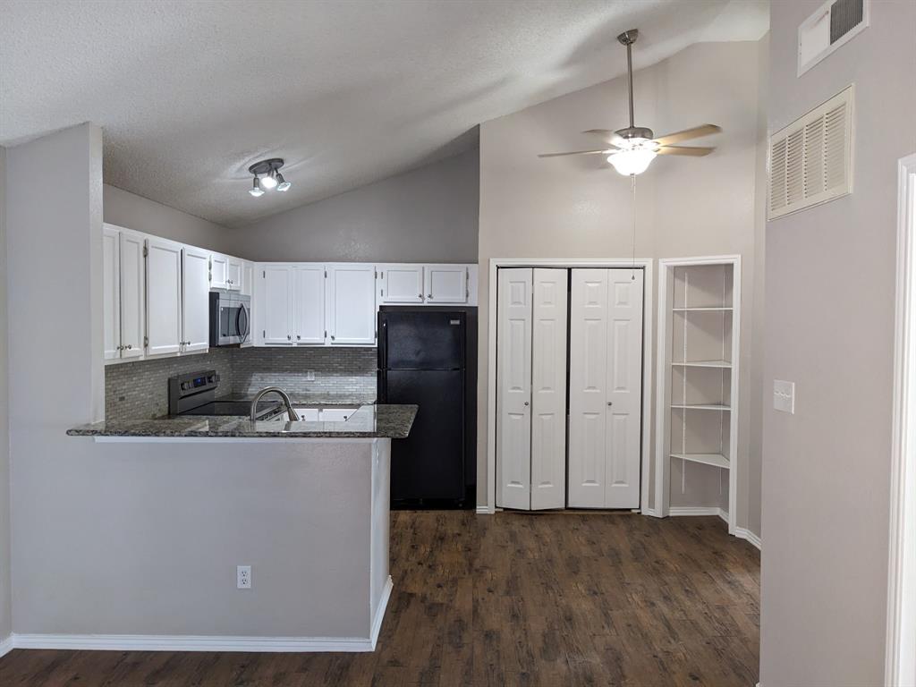 a kitchen with stainless steel appliances granite countertop a refrigerator a sink dishwasher a stove and a dining table with wooden floor