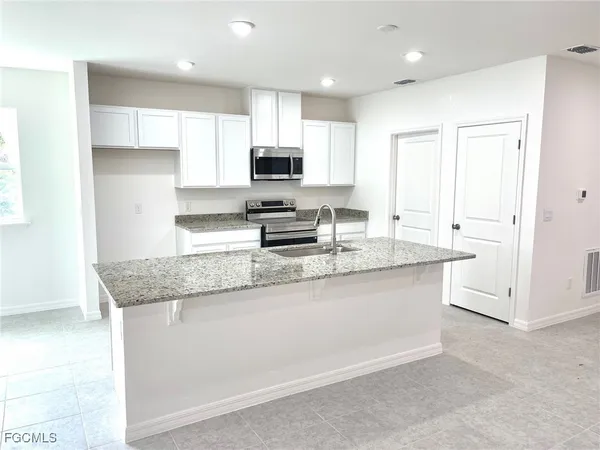 a kitchen with granite countertop a sink a stove a microwave a counter top space and cabinets