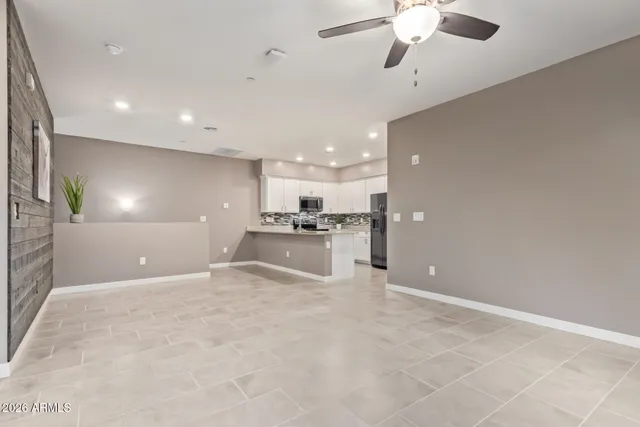 a view of an empty room with kitchen and chandelier fan