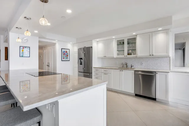 a large kitchen with kitchen island a stove a sink a refrigerator and white cabinets with wooden floor