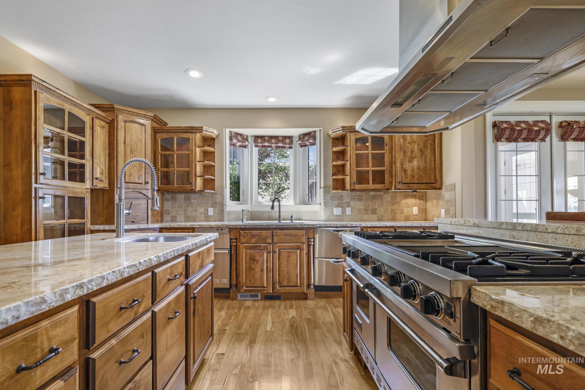 1526 Highway 26 Gooding, ID 83330 - Photo 15 of 48 Kitchen with brown cabinetry, appliances with stainless steel finishes, light stone countertops, extractor fan, and glass insert cabinets