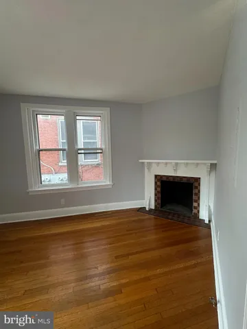 a view of an empty room with wooden floor fireplace and a window