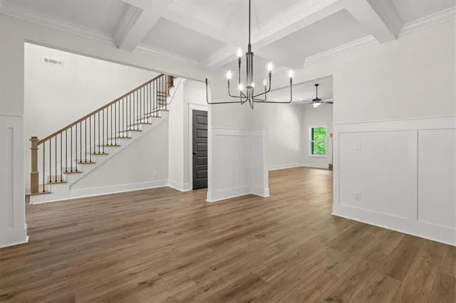 a view of an empty room with wooden floor stairs and a chandelier