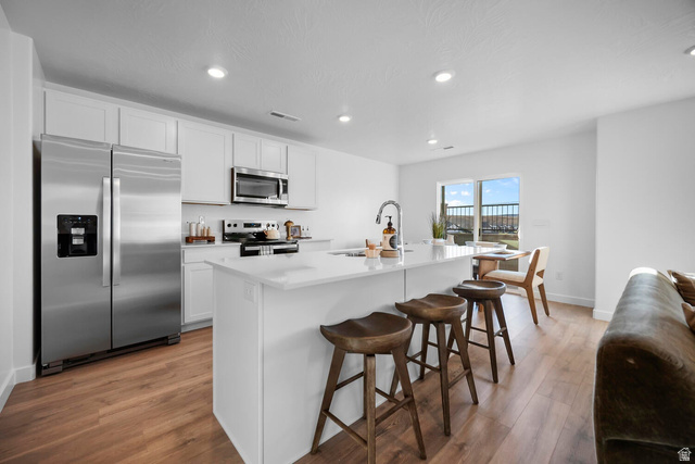 2123 Wolverine Way, Unit 2437 Washington, UT 84780 - Photo 17 of 40 Modern kitchen featuring white cabinetry, stainless steel appliances, a center island with countertop seating, wood-finish flooring, and recessed lighting